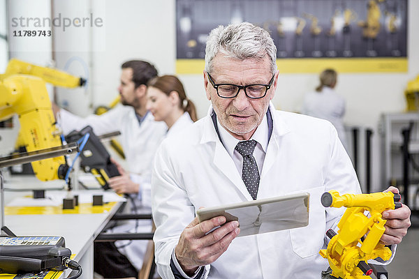 Ingenieur hält Tablette und Modell eines Industrieroboters