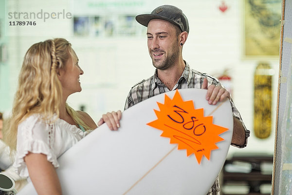 Shop-Assistent  der die Preise für das Surfbrett des Kunden anzeigt