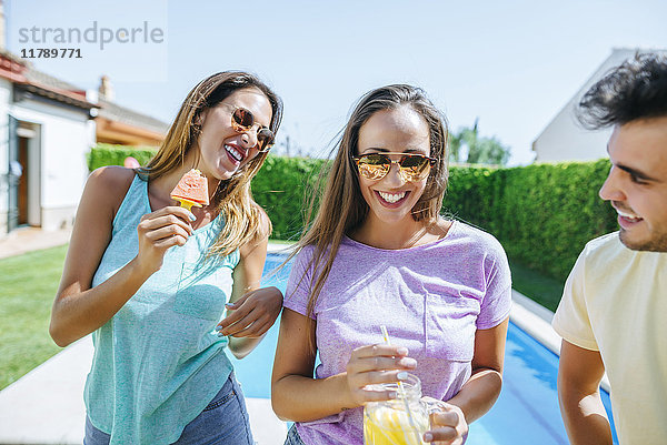 Fröhliche Freunde mit Getränk und Wassermelone am Pool