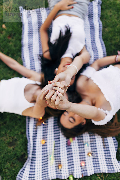 Freunde in einem Park  die auf einer Decke liegen und ihre Arme heben.