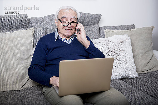 Senior Mann sitzt auf der Couch  mit Laptop und Smartphone