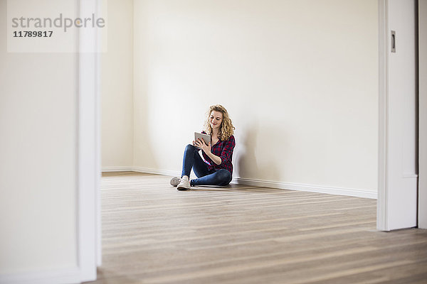 Junge Frau im neuen Zuhause sitzt auf dem Boden mit Tablette