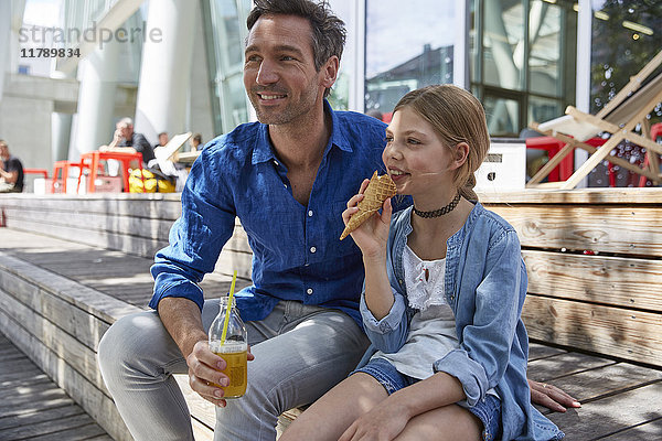 Vater mit Getränk und Tochter mit Eisbecher in einem Outdoor-Café