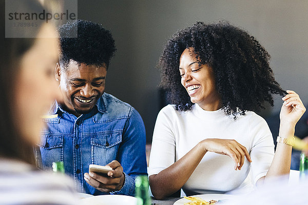 Ein glückliches Paar teilt sich sein Handy am Esstisch.