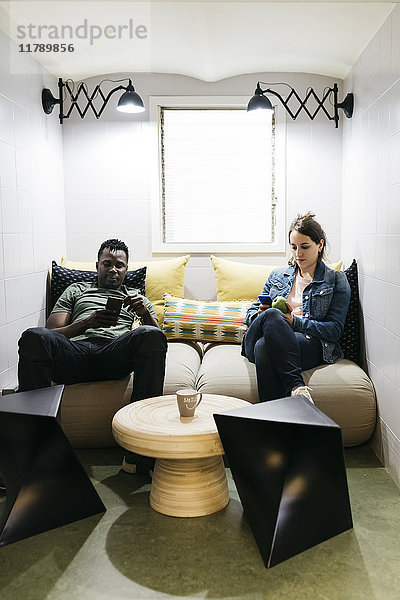 Zwei junge Profis  die mit ihren Smartphones eine Pause im Lehrerzimmer machen.