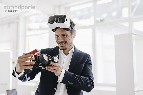 Lächelnder Geschäftsmann mit VR-Brille beim Blick auf Spielzeug-Rennwagen