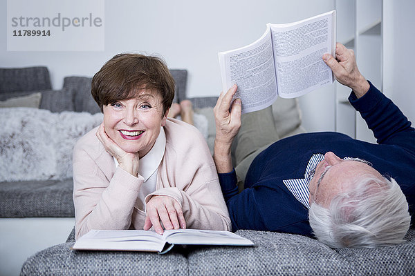 Seniorenpaar auf der Couch liegend  Bücher lesend