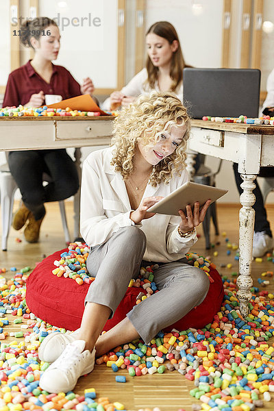 Frau mit Tablette im Büro umgeben von bunten Polystyrolteilen