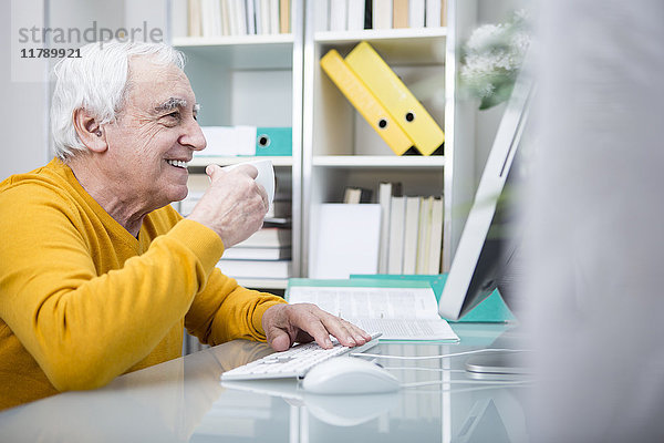 Älterer Mann am Computer bei einer Tasse Kaffee