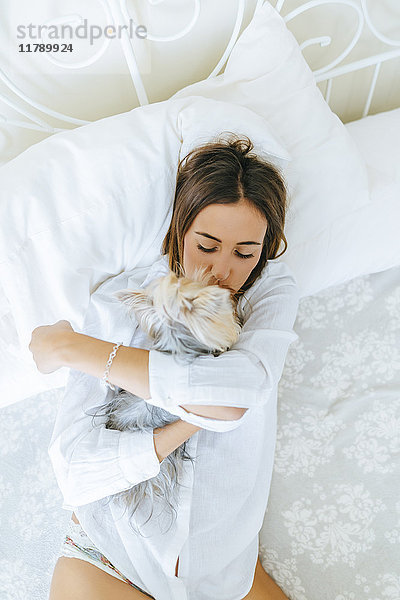 Frau auf dem Bett liegend mit Umarmen und Küssen ihres Yorkshire Terriers  Draufsicht