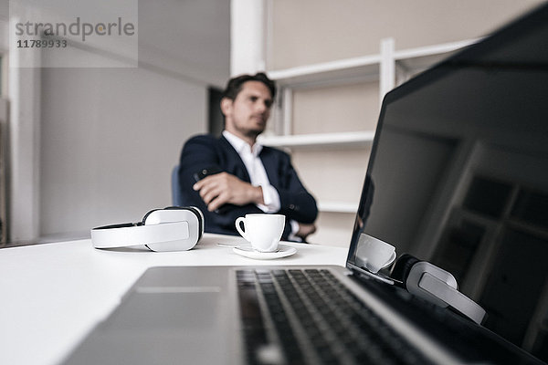 Laptop  Kopfhörer  Kaffeetasse und Geschäftsmann im Hintergrund