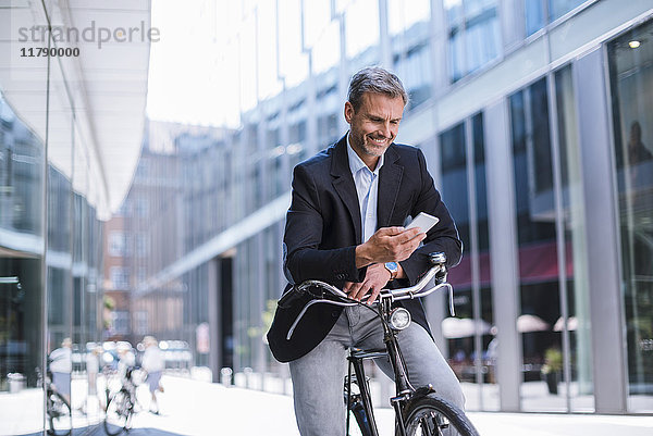 Lächelnder Geschäftsmann mit Fahrrad und Handy in der Stadt