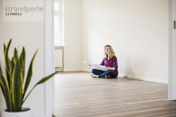 Junge Frau im neuen Zuhause sitzend auf dem Boden mit Plan