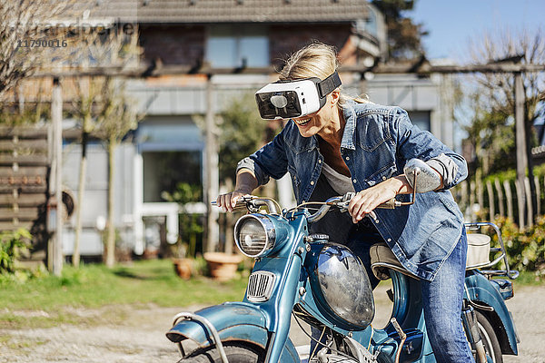 Glückliche Frau auf Oldtimer-Motorrad mit VR-Brille