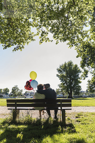 Fröhliches Seniorenpaar mit Luftballons auf der Bank im Park