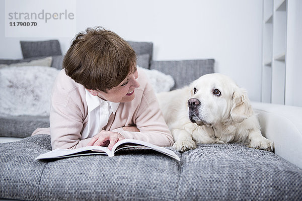 Seniorin auf der Couch liegend  Lesebuch mit Hund an der Seite