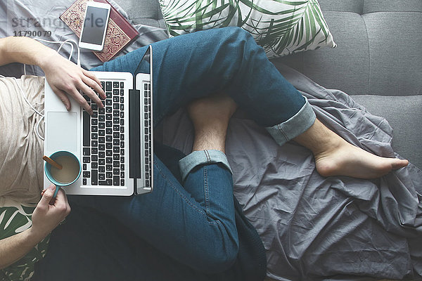 Mann mit Laptop und Kaffeetrinken auf Sofa-Bett  Teilansicht