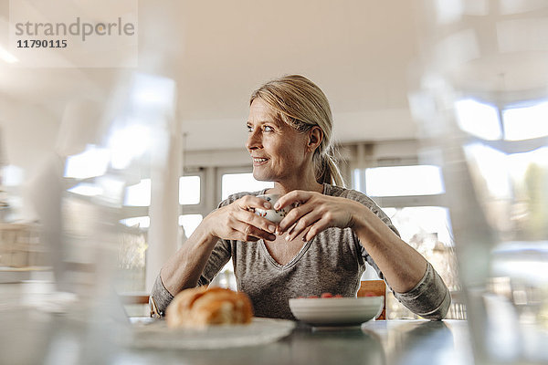 Frau zu Hause beim Frühstücken am Tisch sitzend