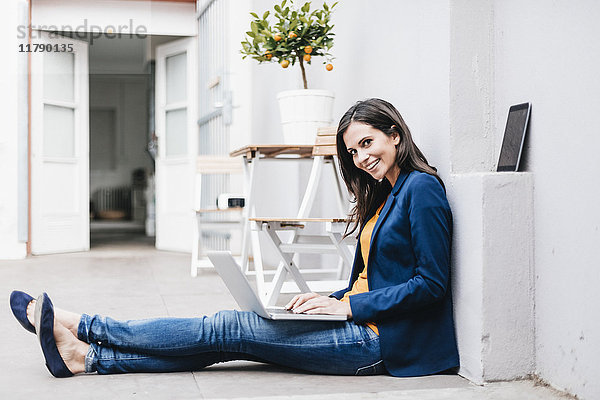 Lächelnde Geschäftsfrau mit Laptop auf dem Boden