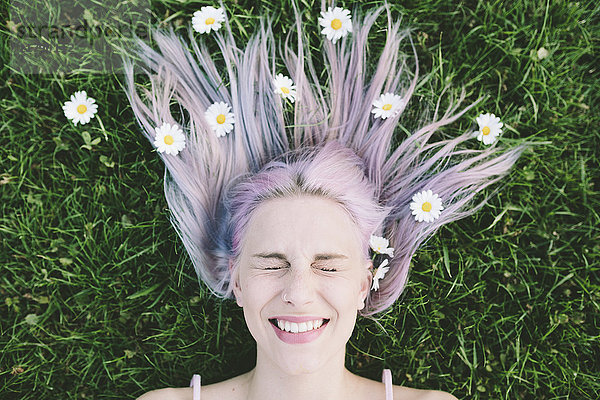 Porträt einer auf Gras liegenden Frau mit geschlossenen Augen und Gänseblümchen auf Haaren