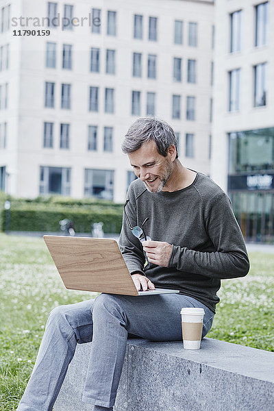 Erwachsener Mann im Freien mit Laptop und Kaffee zum Mitnehmen