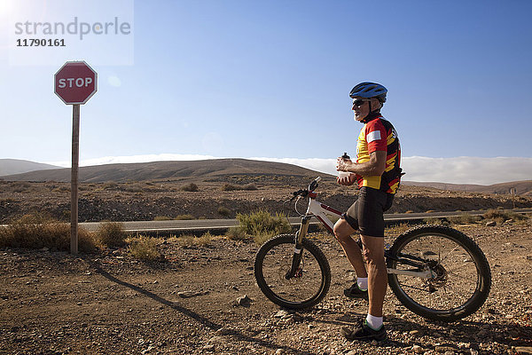 Spanien  Kanarische Inseln  Fuerteventura  älterer Mann mit Mountainbike beim Ausruhen