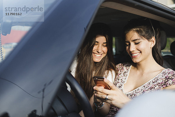 Zwei glückliche junge Frauen  die das Handy im Auto anschauen.