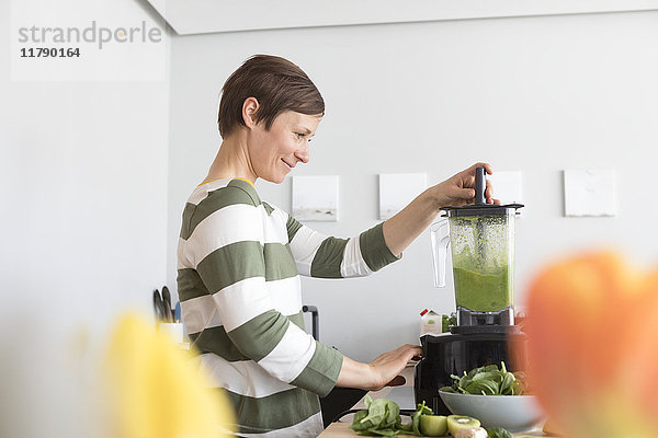 Lächelnde Frau bereitet grünen Smoothie in der Küche vor