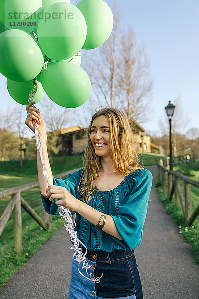 Porträt der lachenden jungen Frau mit grünen Luftballons