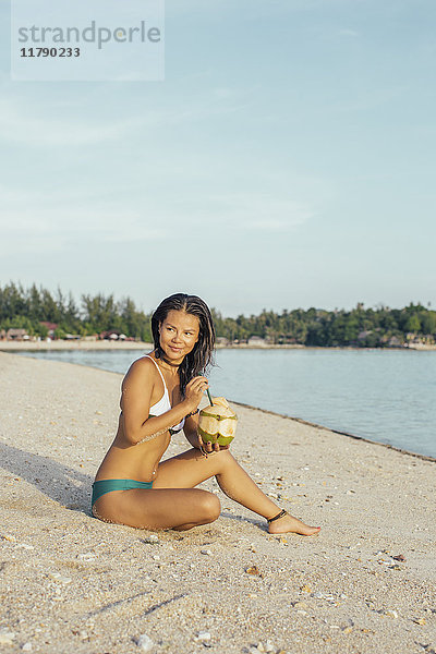 Lächelnde Frau am Strand sitzend mit Getränk