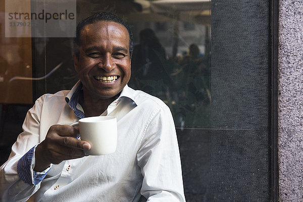 Porträt des lachenden Mannes in einem Café mit Tasse Kaffee
