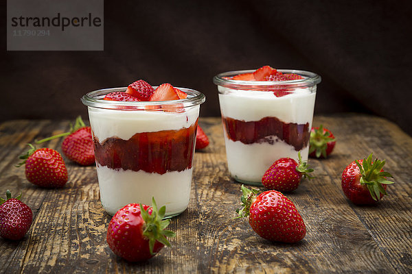 Zwei Gläser griechischer Joghurt mit Erdbeeren auf Holz