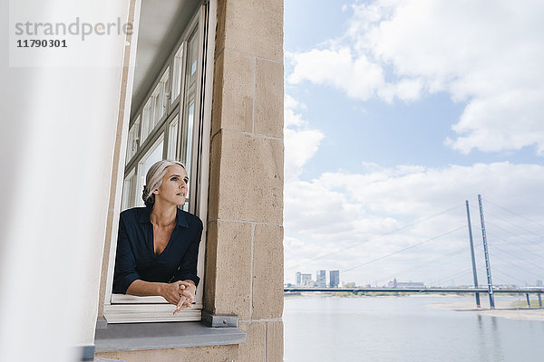 Geschäftsfrau mit Blick aus dem Fenster im Büro am Wasser
