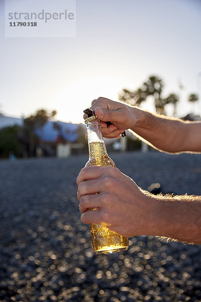 Männerhände öffnen Bierflasche am Strand