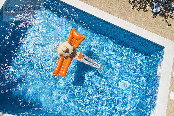 Rückansicht der Frau beim Entspannen auf dem orangefarbenen Luftmatratzenbett im Schwimmbad