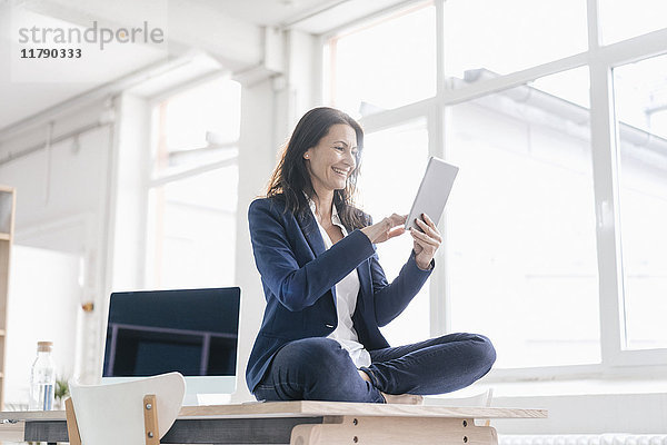 Geschäftsfrau sitzt auf dem Schreibtisch in einem Loft mit Tablette