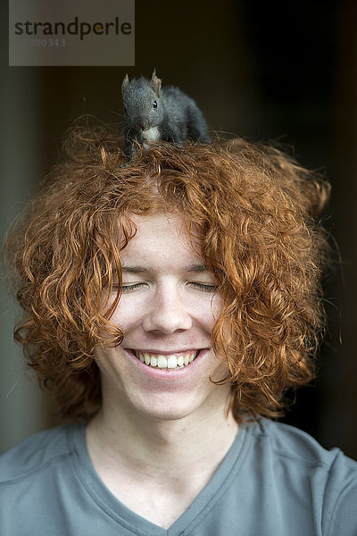 Porträt eines fröhlichen rothaarigen Teenagers mit Eichhörnchen auf dem Kopf