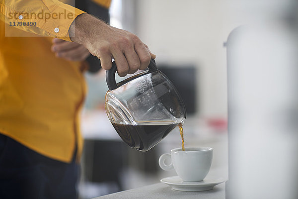 Mitarbeiter mit Schleuder  der bei der Arbeit Kaffee in die Tasse schüttet.