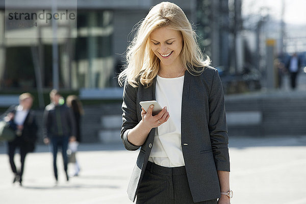 Porträt einer lächelnden blonden Geschäftsfrau beim Blick aufs Handy