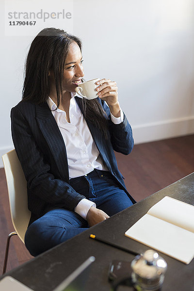 Lächelnde Geschäftsfrau beim Kaffeetrinken während eines Meetings im Büro