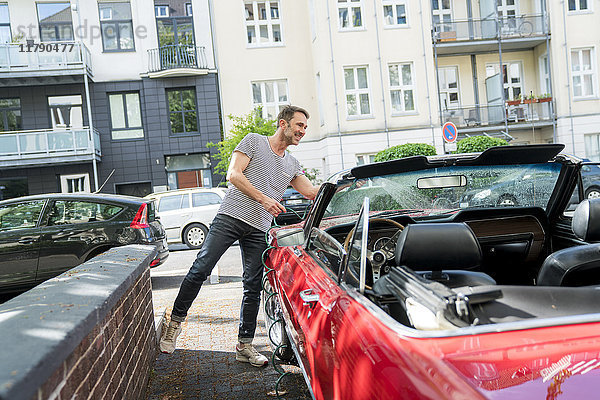 Lächelnder reifer Mann beim Waschen seines Sportwagens