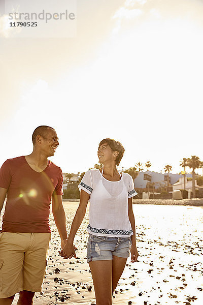 Ein verliebtes Paar geht Hand in Hand am Strand spazieren.
