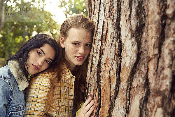 Porträt von zwei jungen Frauen  die sich an den Baumstamm lehnen