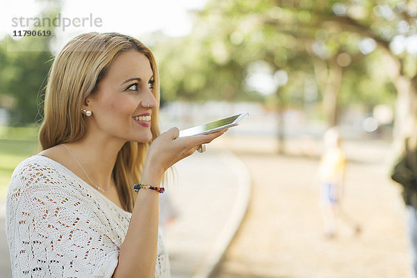 Lächelnde junge Frau mit Handy im Park