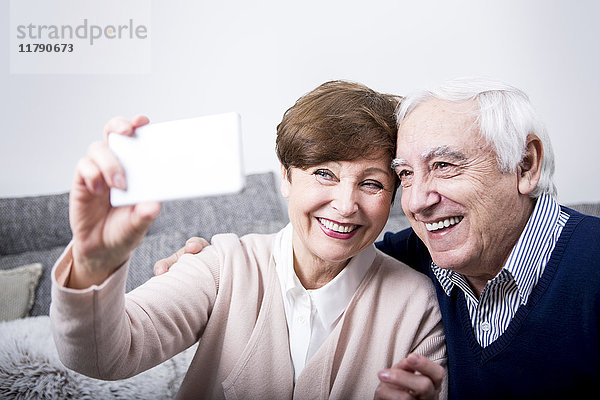 Senior Paar sitzt auf der Couch und nimmt sich ein Smartphone Selfie