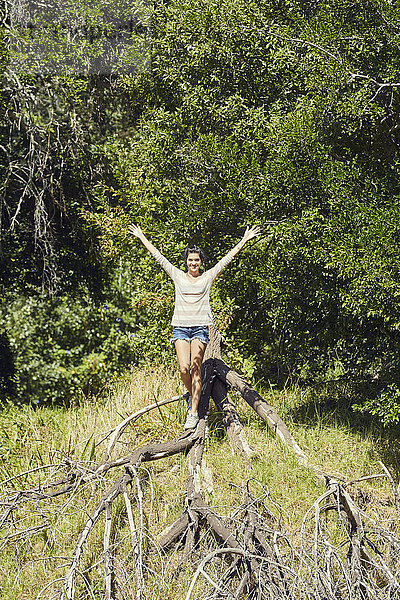 Lächelnde junge Frau balanciert auf Baumstamm