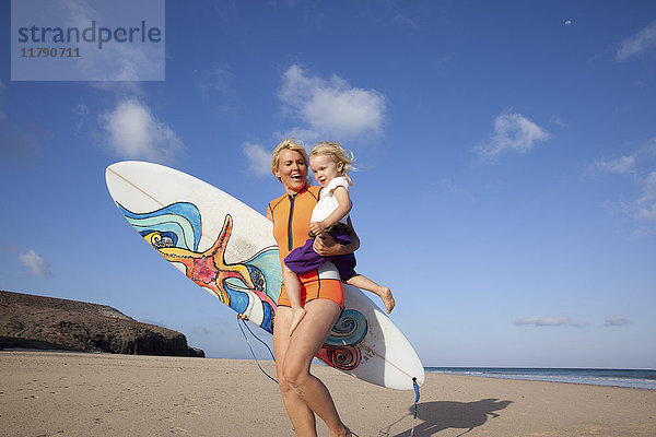 Spanien  Fuerteventura  glückliche Mutter und Tochter beim Spaziergang mit Surfbrett am Strand