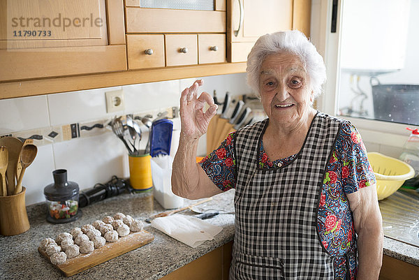 Porträt einer lächelnden Seniorin mit ok-Zeichen in der Küche