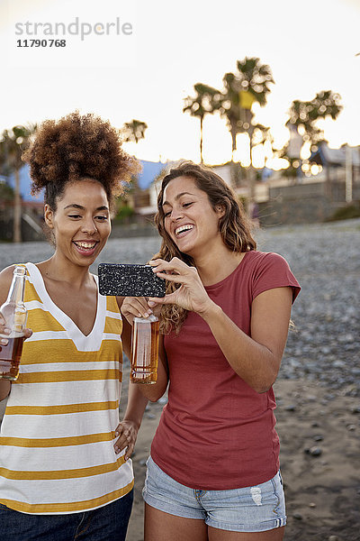 Zwei lachende Freunde mit Bierflaschen  die Selfie am Strand mitnehmen.