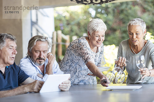 Zwei ältere Frauen decken den Tisch auf der Terrasse  während ihr Mann die Tablette benutzt.